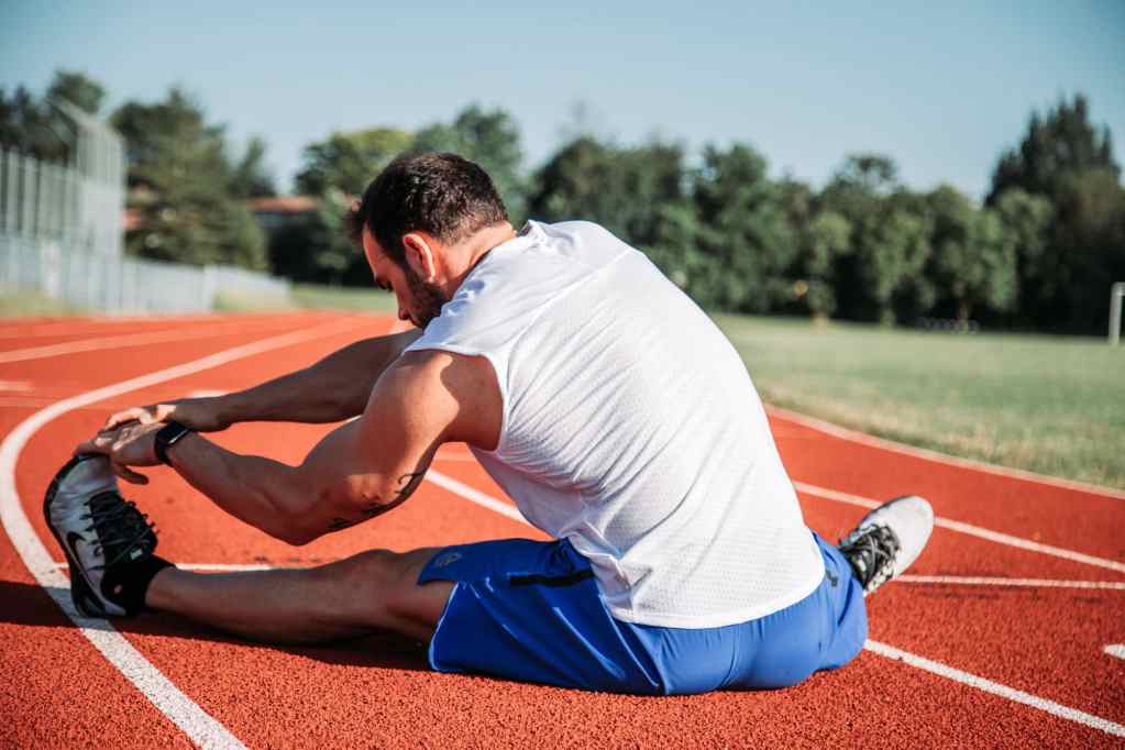 Man stretching while sat on running track